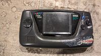 Front view of Sega Game Gear showing screen, control pad, buttons, and wear/residue on housing.