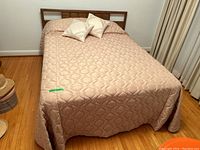 Full bed setup showing wood headboard, mattress covered with light pink quilted bedspread and three matching pillows.