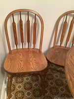 Front view of two oak dining chairs showing spindle backrest and contoured seat.