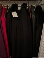 Photo of six ladies' overcoats hanging on hangers showing various dark colors and fur collars.