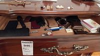 Wide view of lot items on wooden surface including wallets, pens, cufflinks, razor, watch, keychain