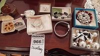 Overview of jewelry lot showing MOD watch with worn metal band, various bracelets including silver-tone and beaded types, multiple pairs of earrings including black and white geometric style, a floral pin, pill box, and brooch.