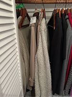Image showing clothes hanging in closet, including two beige coats and a knit sweater jacket.