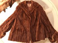 Photo showing brown mink fur coat spread flat on a white door, detailing the wide collar and cuffs.