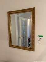 Full view of the rectangular wall mirror hanging on a white wall, showing beveled glass edge and gilt decorative frame with floral and scroll detailing.