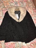 Full view of the black Persian lamb jacket with light mink collar laid on floral bedspread.