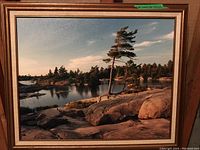 Full view of one of the framed photographic landscape prints showing rocky shoreline, pine trees and water at dusk