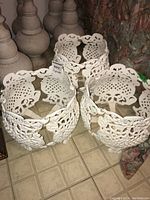 Three white metal garden planters with ornate lattice and scrollwork design arranged closely on a tiled floor, photographed from above and side angles.