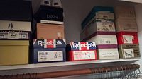 Boxes of assorted shoes piled on shelves showing brand labels and sizes