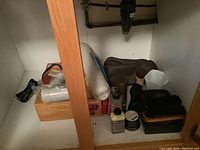 Shoeshine kit items inside a small cabinet including brushes, shoe polish containers, and applicators along with hairdryers and bath mat.