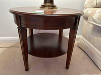 Front view of the round wood side table showing lower shelf and tapered legs