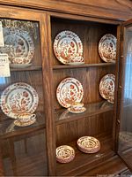 Wooden china cabinet with multiple Spode India Tree dinner plates, tea cups and saucers displayed across shelves
