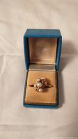 Gold ring with four white pearls in a cluster setting displayed in a blue jewelry box with beige interior.