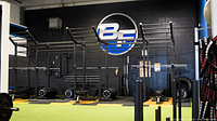 Functional training area with multi-station rig, barbells, weight plates, BC logo on wall
