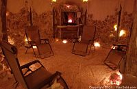 Salt cave interior with walls, floor, and lounge chairs for therapy sessions, lit with salt lamps.