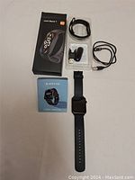Apex Fit smartwatch and accessories arranged on a white surface including black fitness watch with strap, USB charging cable, heart rate monitor clip, user manual and original box.