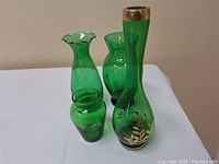 Four green glass vases of different shapes and sizes shown on a white surface against a beige background.