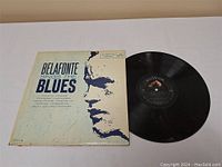 Vinyl record with cover featuring stylized image of Harry Belafonte and text "Belafonte Sings The Blues" along with the record disk partially out of sleeve.