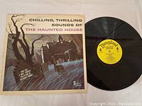 Photo of the vinyl record with cover showing eerie haunted house artwork and lightning. The Disneyland yellow label is visible on the black vinyl.