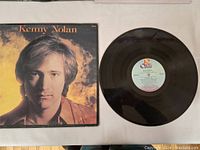 Photo of the LP record and cover laid flat, showing the black vinyl disc and the album cover with Kenny Nolan's portrait.