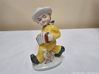 Front right angle view of the figurine showing the boy playing accordion with chicken at feet.