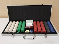 Poker chips of multiple colors, two dice, buttons, and playing cards in open aluminum case.