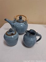 Photo showing all three pieces in the set: teapot, creamer, and sugar bowl on white cloth background.