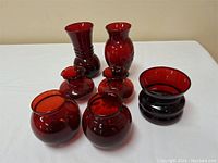 Six red glass items including vases and bowl arranged on a white surface.