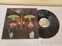 Vinyl LP record partially out of album cover laid flat on a white surface showing vinyl and cover front