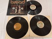 Three vinyl LP records including one with the cover "The Best of Bread Volume Two" and two others without covers.