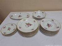 Front view of the full china set showing various plates, bowls, and serving dishes with floral pattern and gold accents.