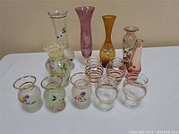 Front view of entire glassware lot showing all vases and glasses on white tablecloth