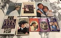 Top-down photo showing all 8 royal books arranged on marble surface, covers visible with titles and images of Prince Charles, Princess Diana and other royal themes.