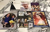 Six books and magazines arranged on marble surface, showing front covers featuring British royals including Queen Elizabeth II and Kate & William.