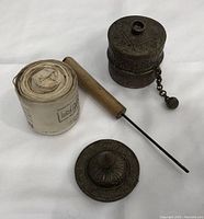 Prayer wheel body separate from handle with engraved lid and rolled parchment displayed beside them on white background