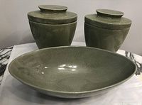 Three ceramic pieces on white cloth: two lidded jars and one large oval vase in green crackle glaze
