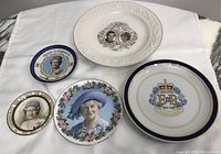Set of five decorative plates featuring British royalty, laid out on a white cloth. Plates vary in size from 4 to 10 inches and depict various members of the royal family with commemorative text and ornate borders.