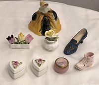 Overview of china trinket holders, floral arrangements, decorative shoes, and figurine on white surface