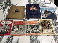 Seven vintage royalty-related books and pamphlets arranged on marble surface, includes notable torn dust jacket on one book.
