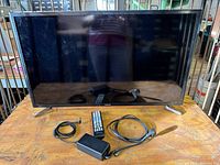 Front view of 32-inch Samsung smart TV on wooden surface, with remote and cables in front.