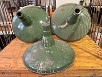 Three green enamel industrial light shades placed on a wooden surface.