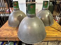 Front view of three industrial hanging lights with green enamel bases and large aluminum shades on wooden surface.