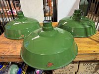 Three matching dark green enamel shades with white interior placed on a wooden surface.