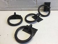 Four steel ring hooks each with 4 inch diameter rings, attached to square mounting plates with two screw holes
