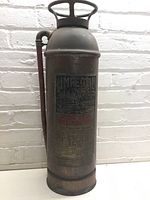 Front view of an antique Imperial fire extinguisher showing the top handle, label, and aged metal body with visible text and rust.