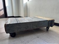 Side view of the antique wooden dolly showing aged wood planks and caster wheels.