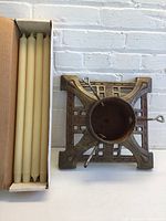 Box of eight long, off-white taper candles next to an antique metal Christmas tree base with rust and adjustable screws.