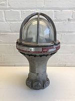 Front view of the heavy-duty industrial light fixture showing metal cage, glass dome, and base