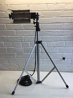 Full view of the halogen light mounted on a silver tripod, showing the height adjustability and tripod construction.