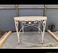 Full view of round metal patio table with decorative painted metal frame and visible wear and rust.